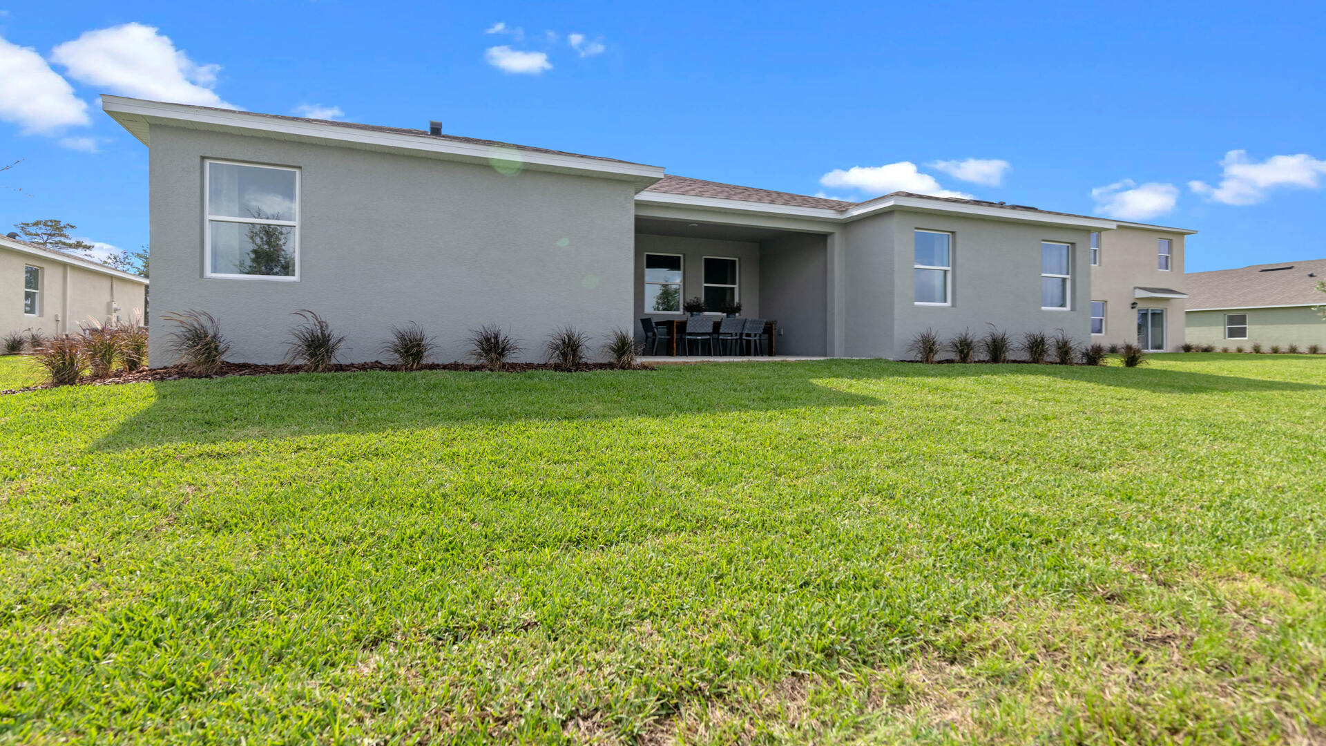 Rear of home with view of grassed backyard, porch seating and slider glass doors.