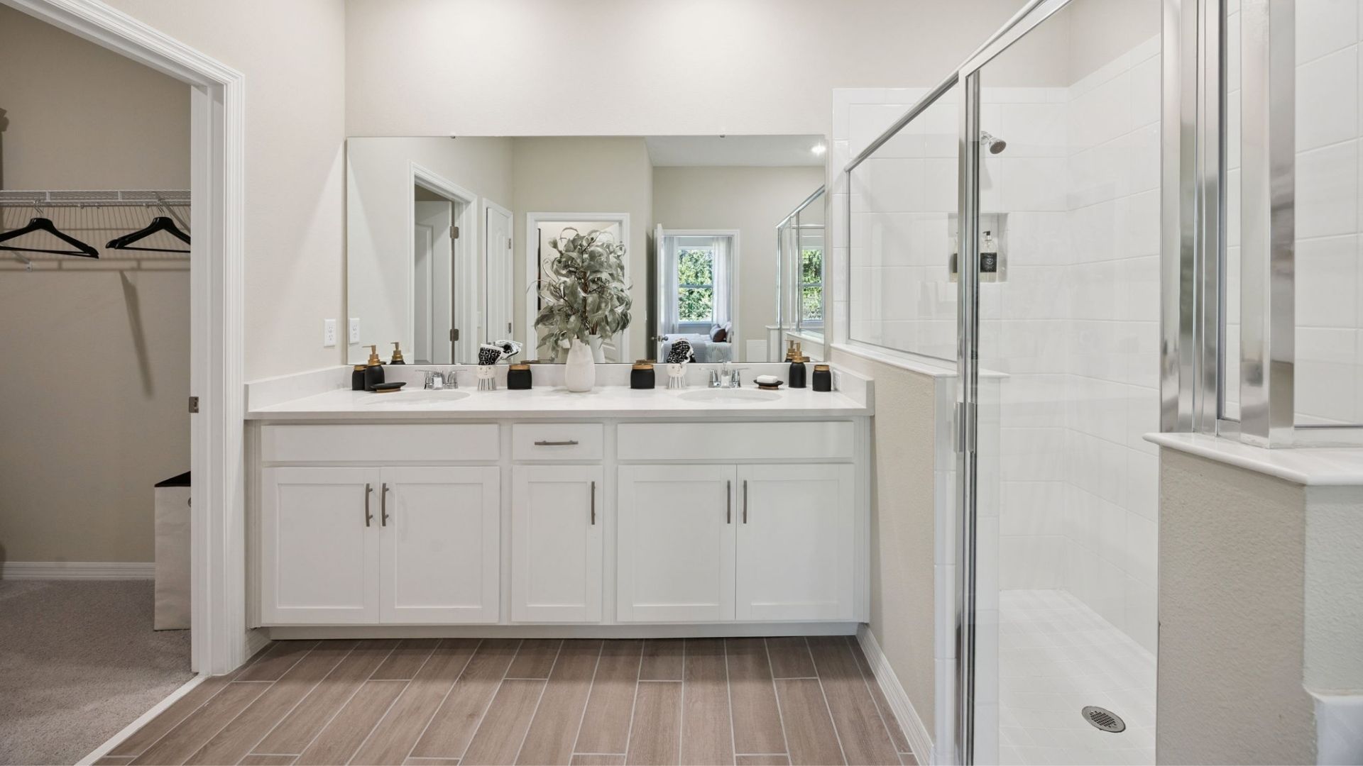 Modern primary bathroom with double vanity countertops with granite, cabinets and large wall mirror.