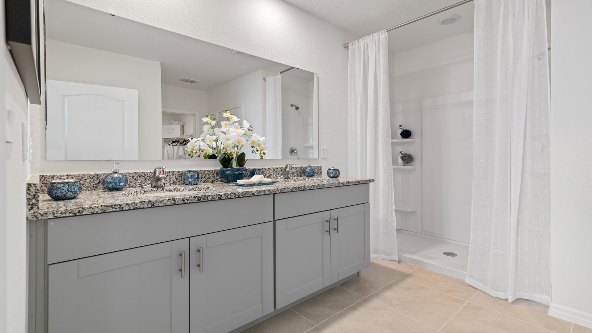 Modern bathroom with double vanity sinks, large wall mirror, cabinets and granite countertops.