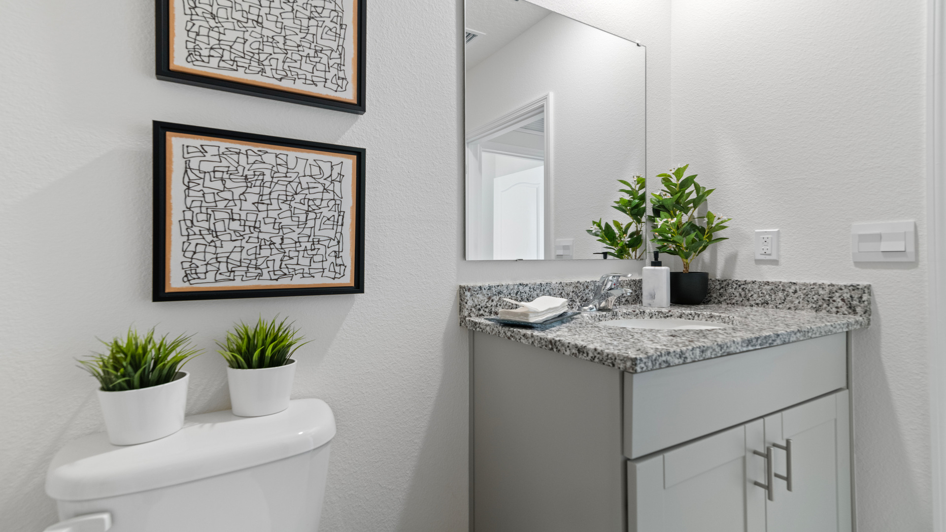 Modern bathroom with single bowl sink, granite vanity, wall mirror, cabinets and toilet.