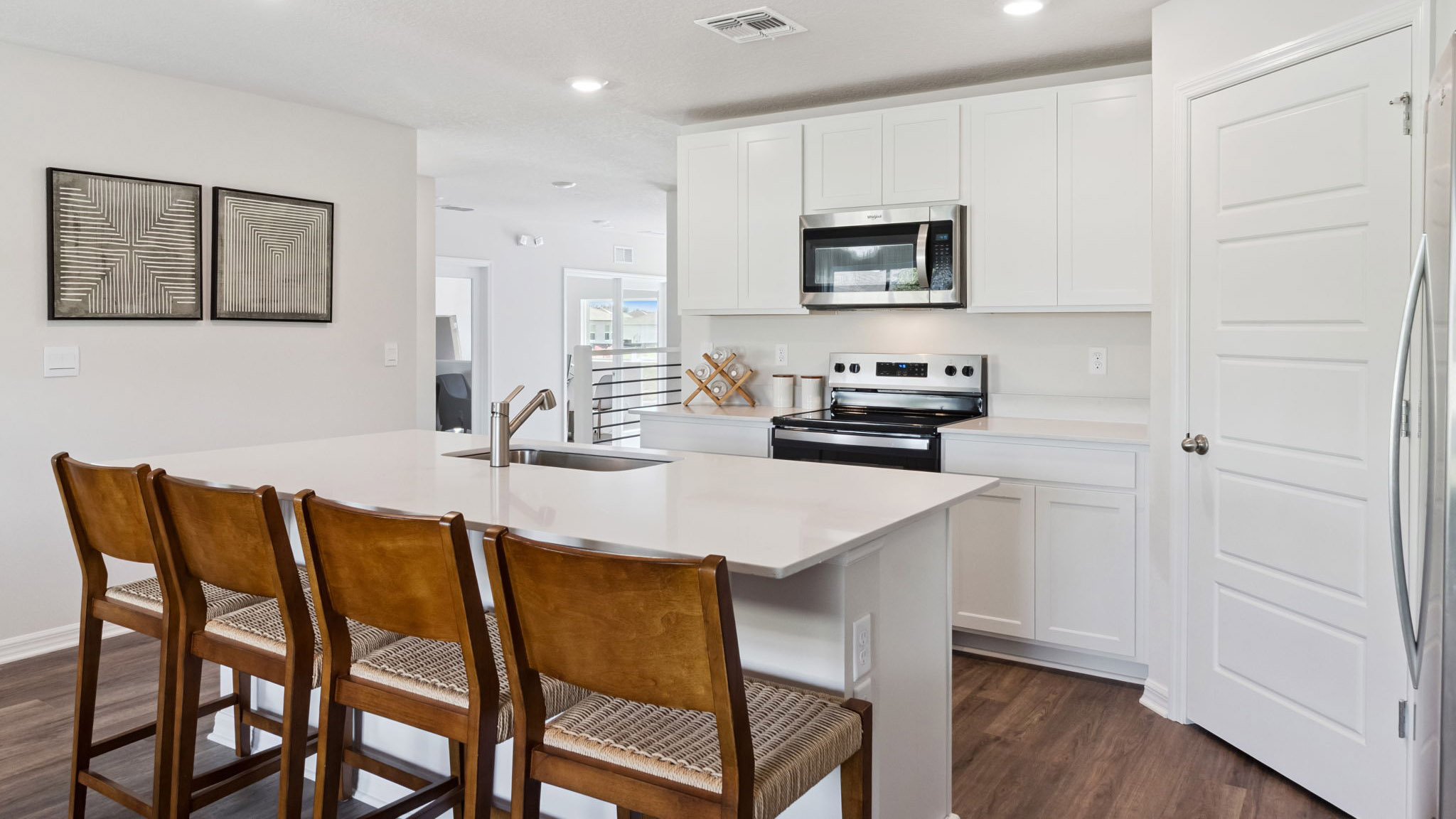 Kitchen with island seating, quartz counters, spacious pantry and stainless steel appliances showing entry way to home overseeing living area.