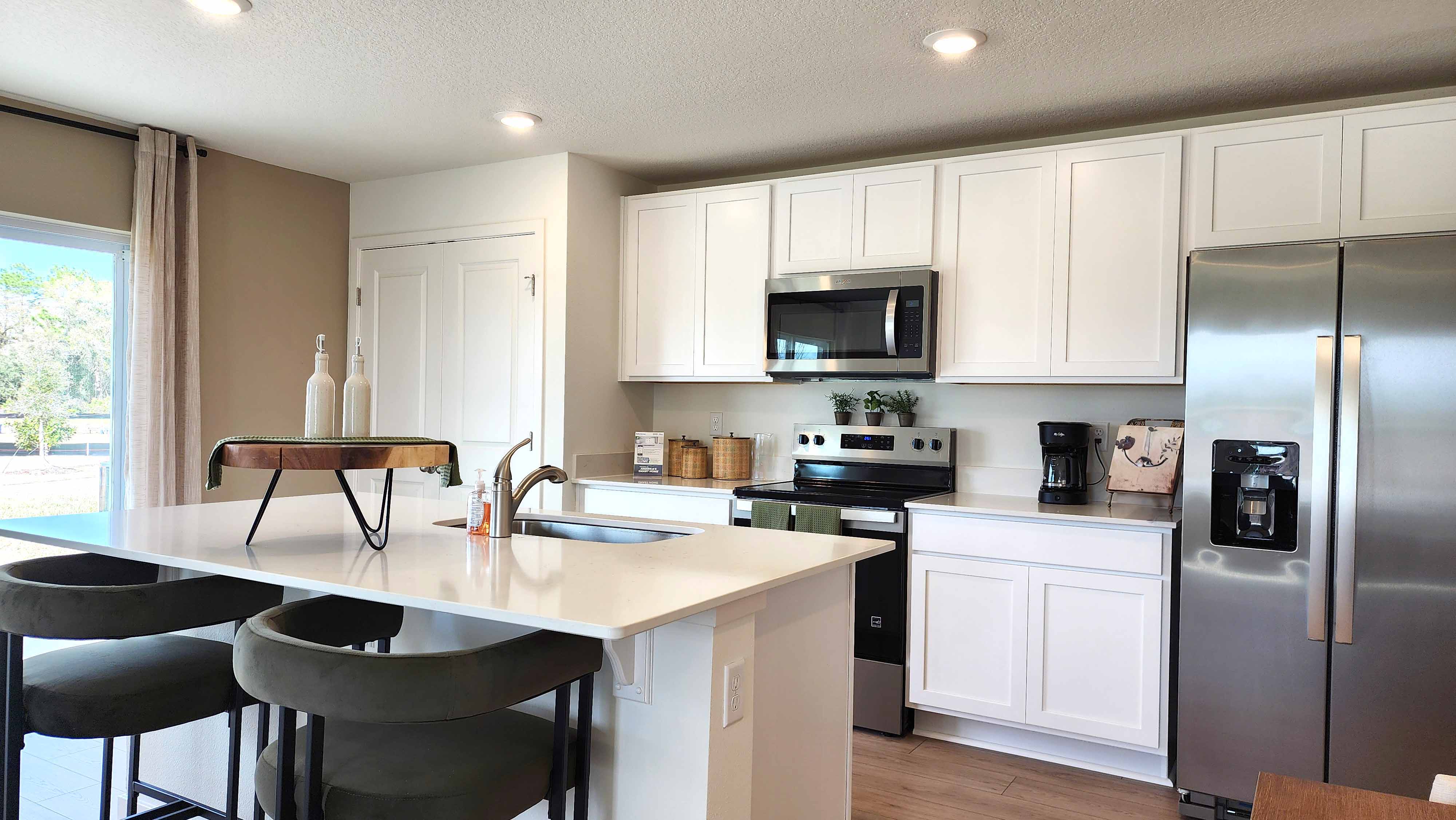 Kitchen with island seating, quartz counters, spacious pantry and stainless steel appliances.