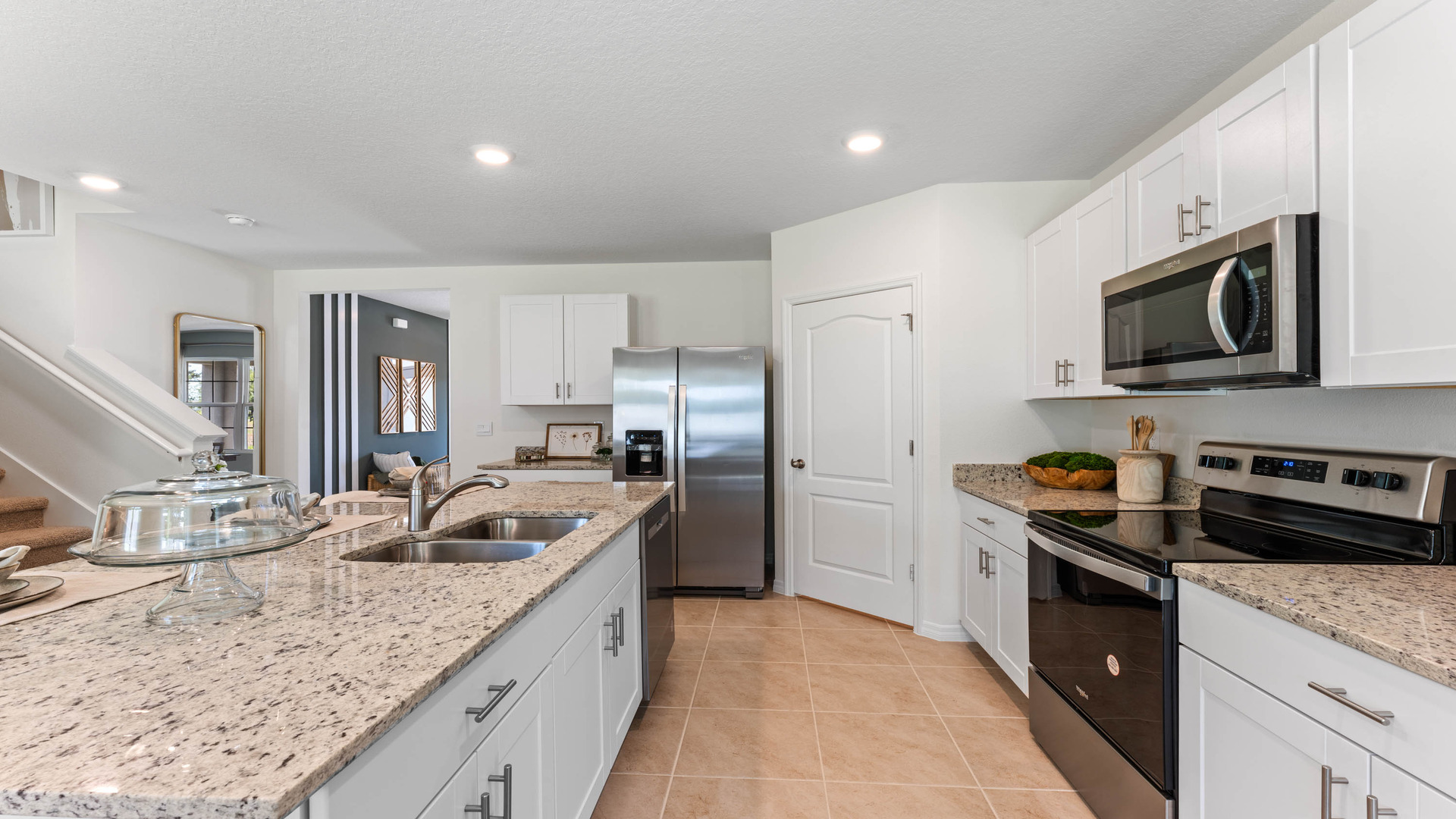 Kitchen with island seating, granite counters, spacious pantry and stainless-steel appliances overseeing staircase and living area.