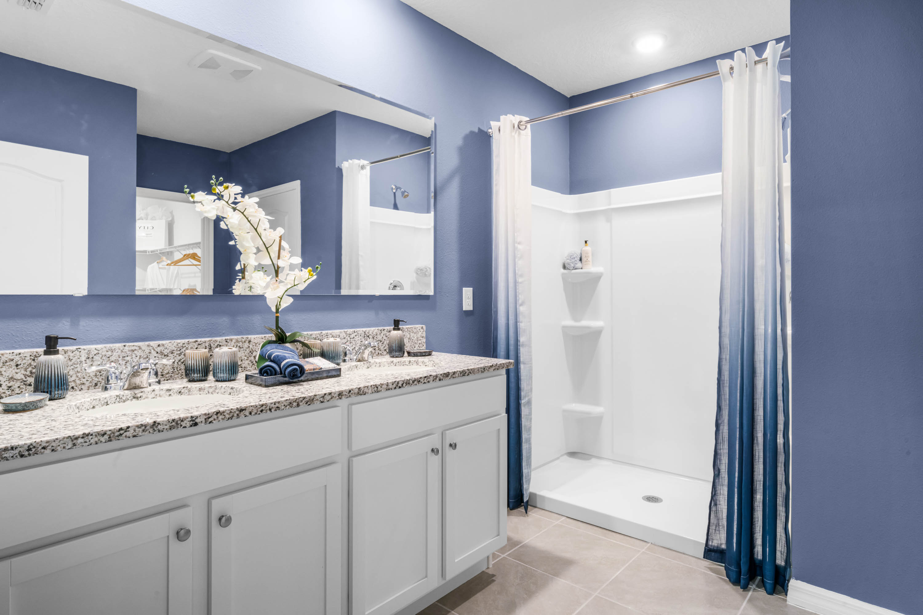 Modern bathroom with double vanity, large wall mirror, cabinets and granite countertops along with walk-in shower.