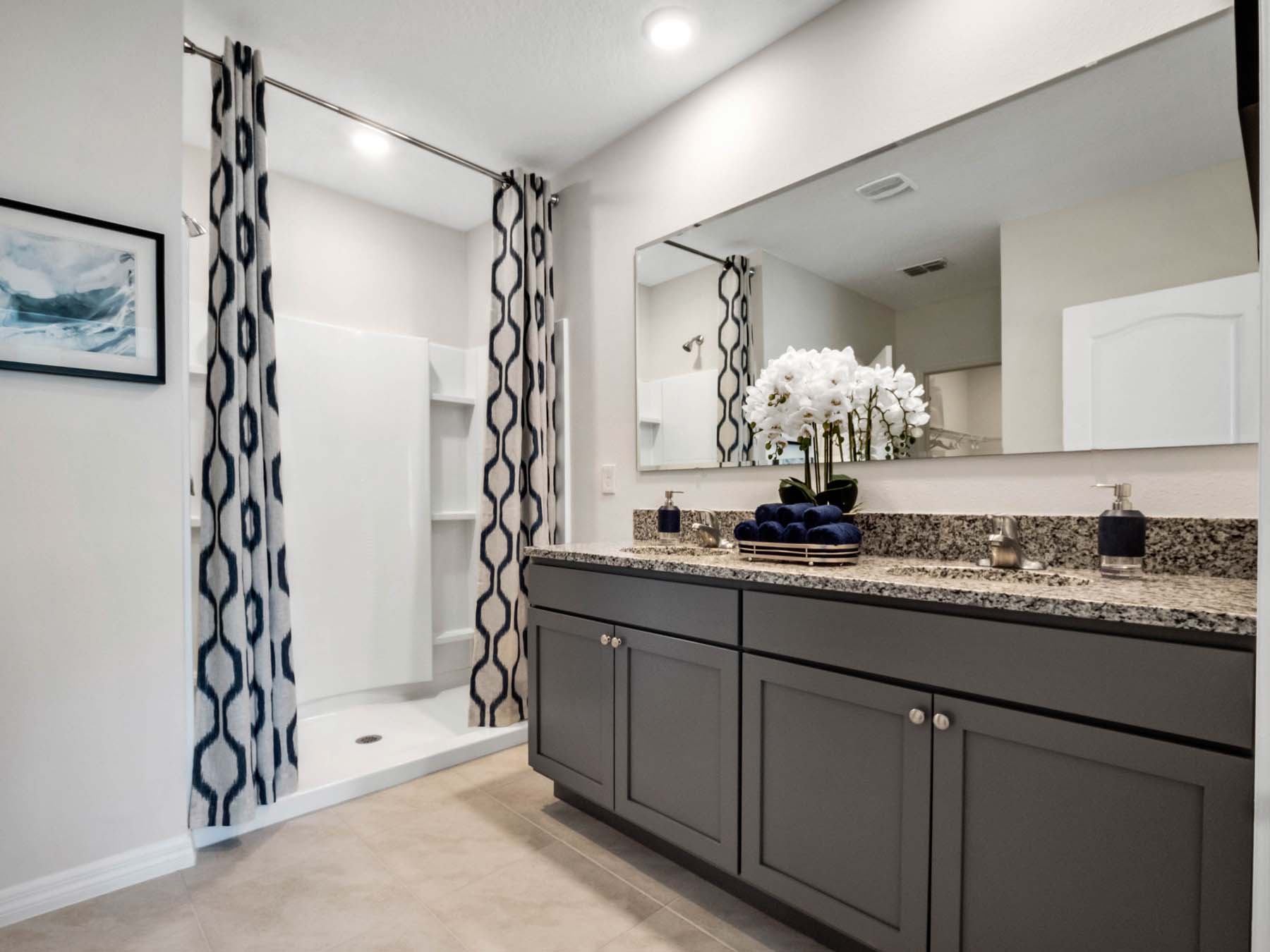 Modern bathroom with double vanity, large wall mirror, cabinets and granite countertops along with walk-in shower