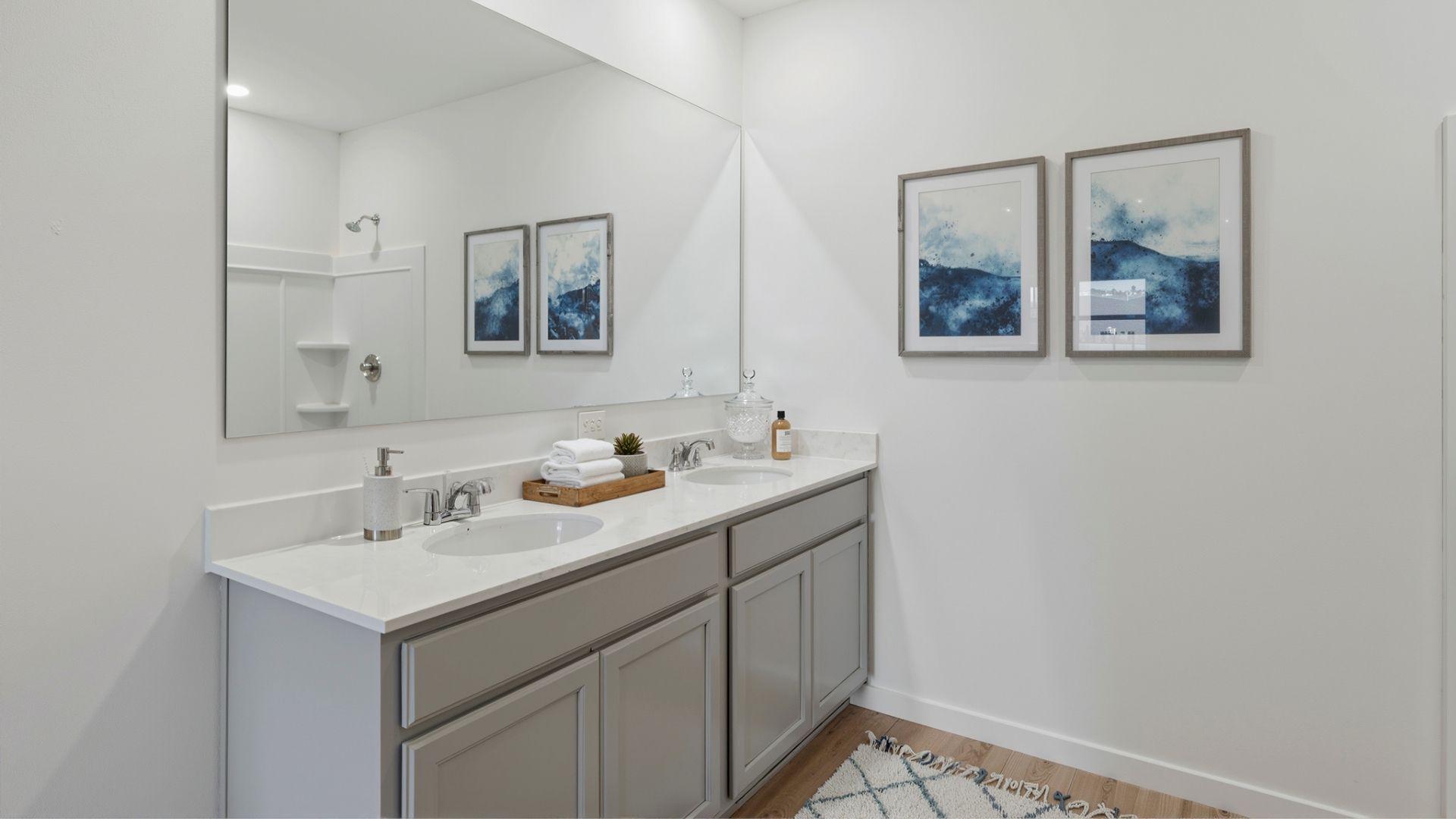 Modern bathroom with double vanity, large wall mirror, cabinets and quartz countertops along with walk-in shower