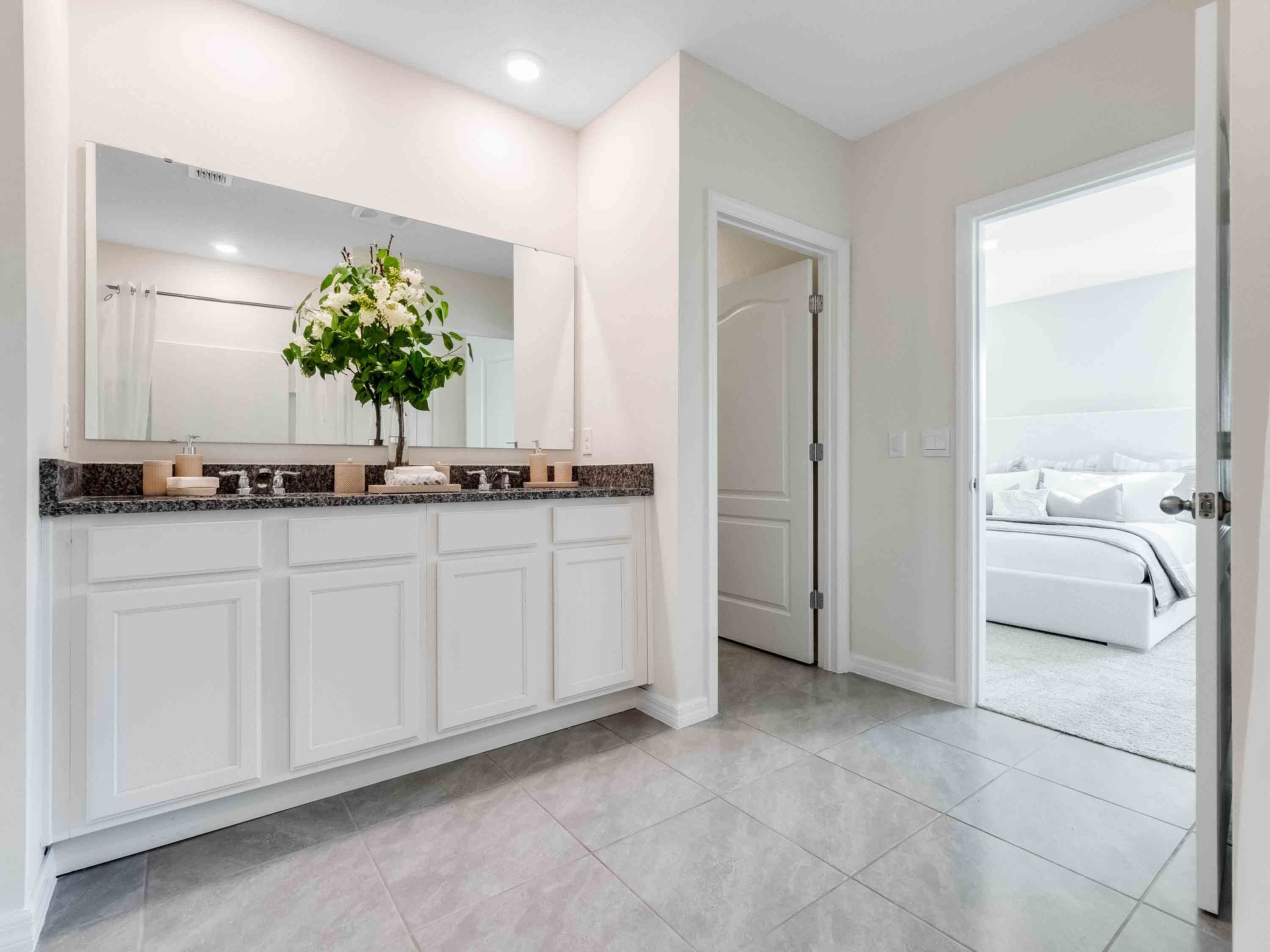 Modern bathroom with double vanity sinks, large wall mirror, white cabinets and granite countertops.