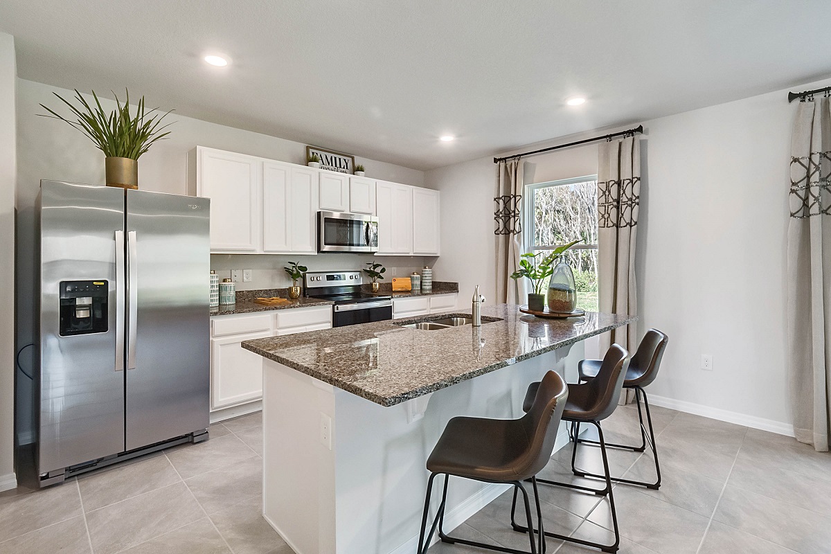 Kitchen with island seating, quartz counters, spacious pantry and stainless steel appliances showing entry way to home overseeing living area.