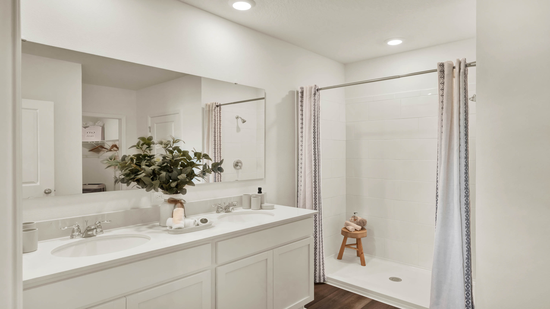 Modern bathroom with double vanity, large wall mirror, cabinets and quartz countertops along with walk-in shower
