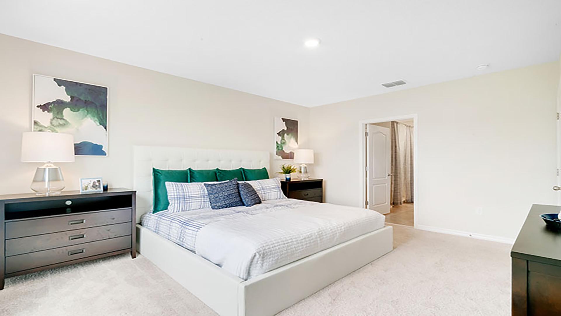 Spacious primary bedroom with king size bed, carpet flooring, natural lighting.