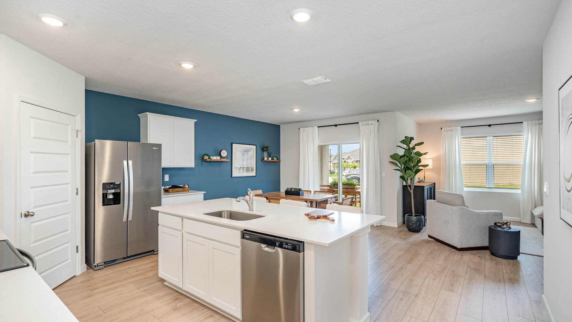 Modern kitchen with stainless steel appliances, white cabinets, and a blue accent wall, leading to a cozy dining area and living space.