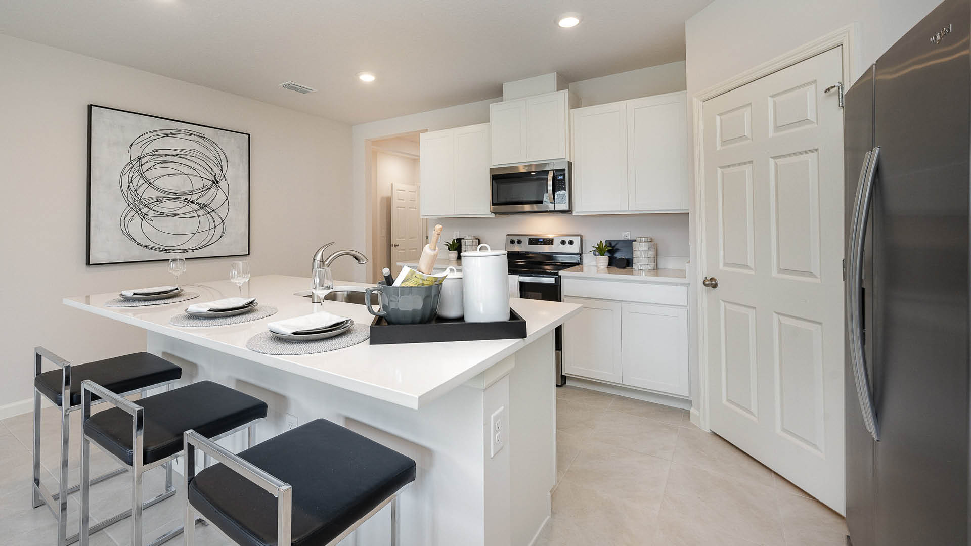 Modern kitchen featuring white cabinets, stainless appliances, minimalist decor, and a sleek island with black bar stools.