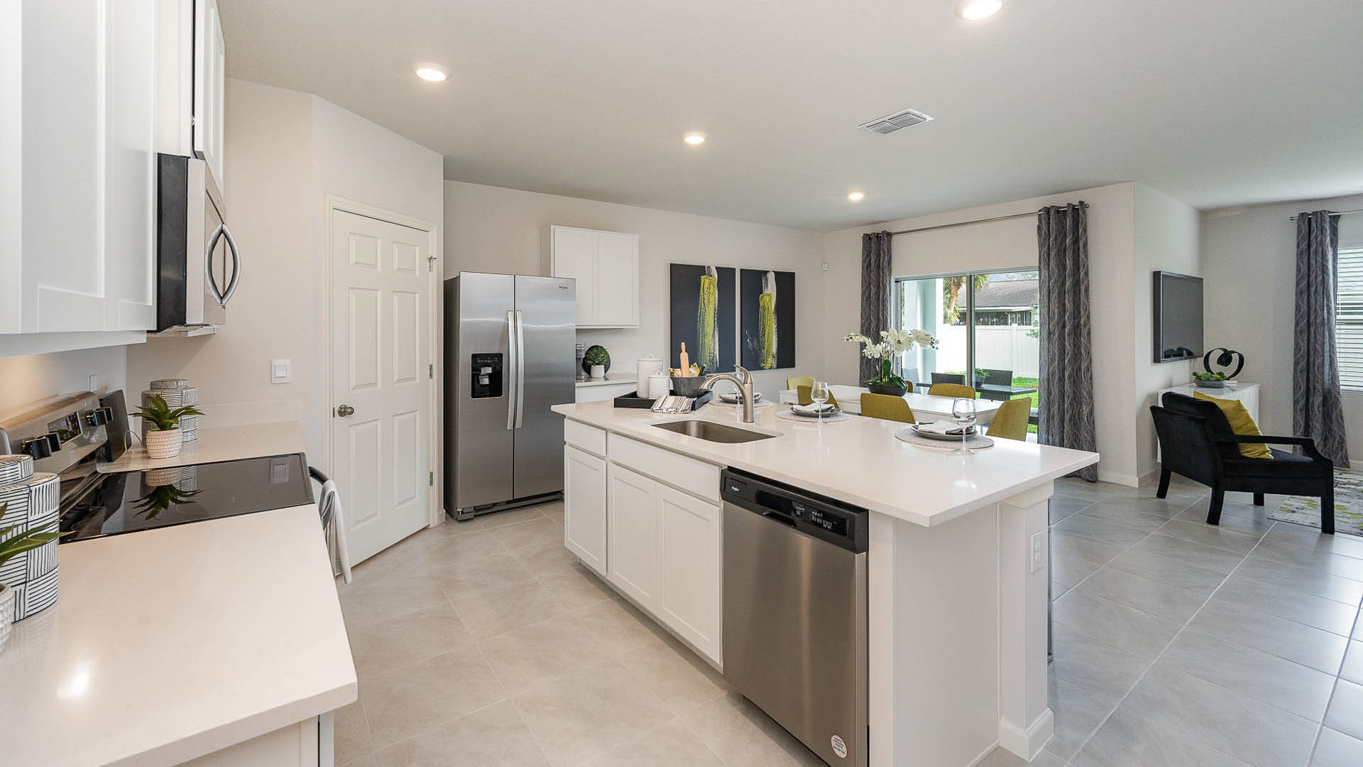 Bright and modern kitchen with white cabinets, stainless steel appliances, and open dining area featuring a glass table and green accents.