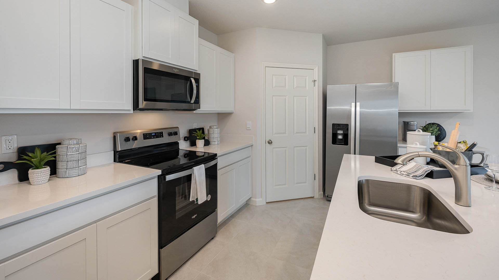 Modern kitchen with white cabinets, stainless steel appliances, and a sleek countertop featuring a sink and decorative plants.