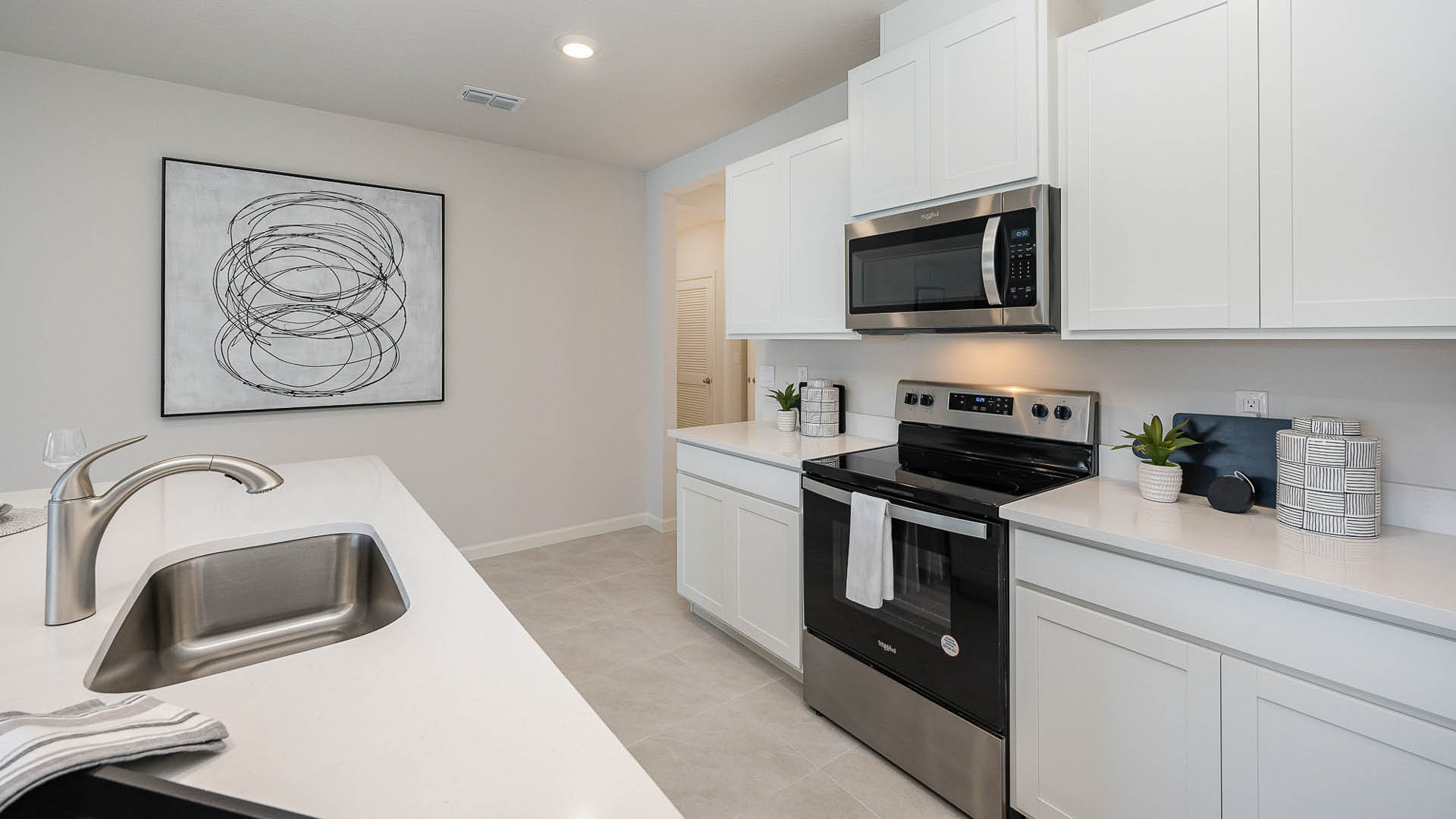 Modern kitchen featuring white cabinetry, stainless steel appliances, a sleek sink, and minimalist decor with a wall art piece.
