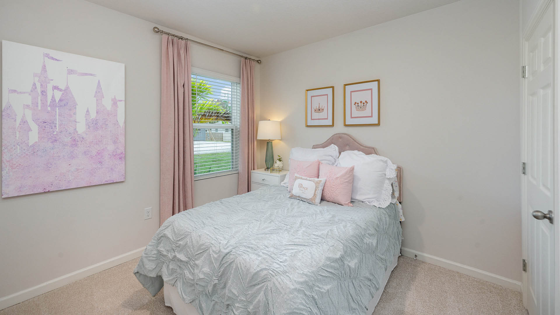 Cozy bedroom featuring a pastel themed decor with a plush bed, pink curtains, and whimsical castle artwork on the wall.