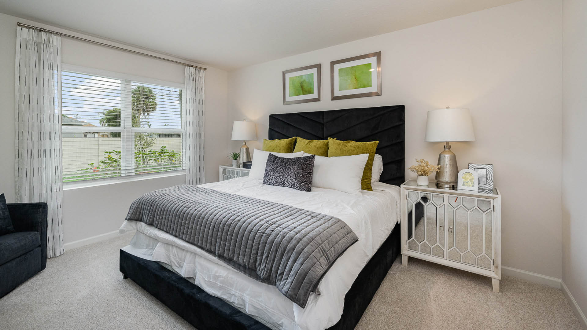 Cozy bedroom featuring a black tufted headboard, plush bedding with green accents, modern nightstands, and natural light from a large window.