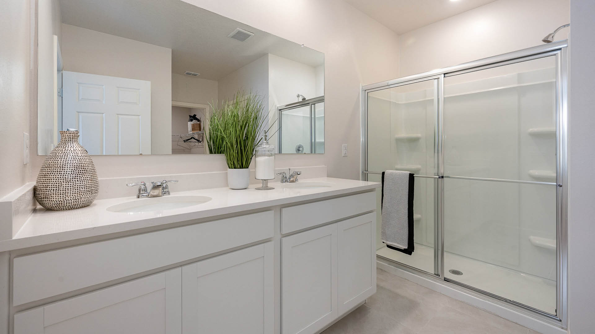 Modern bathroom with dual sinks, a glass shower, and stylish decor featuring a potted plant and decorative vase.