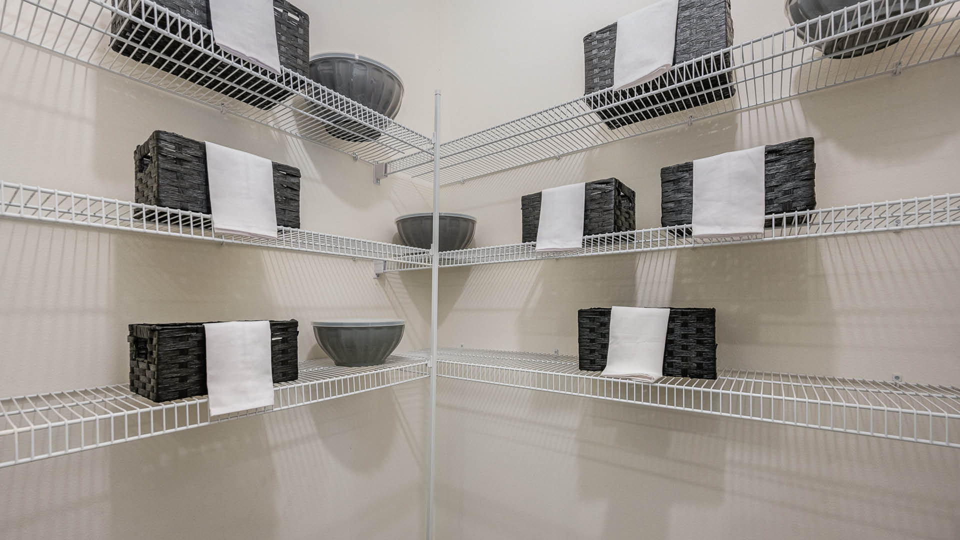 Organized pantry shelves feature dark woven baskets with white labels and gray bowls, all neatly arranged in a bright space.
