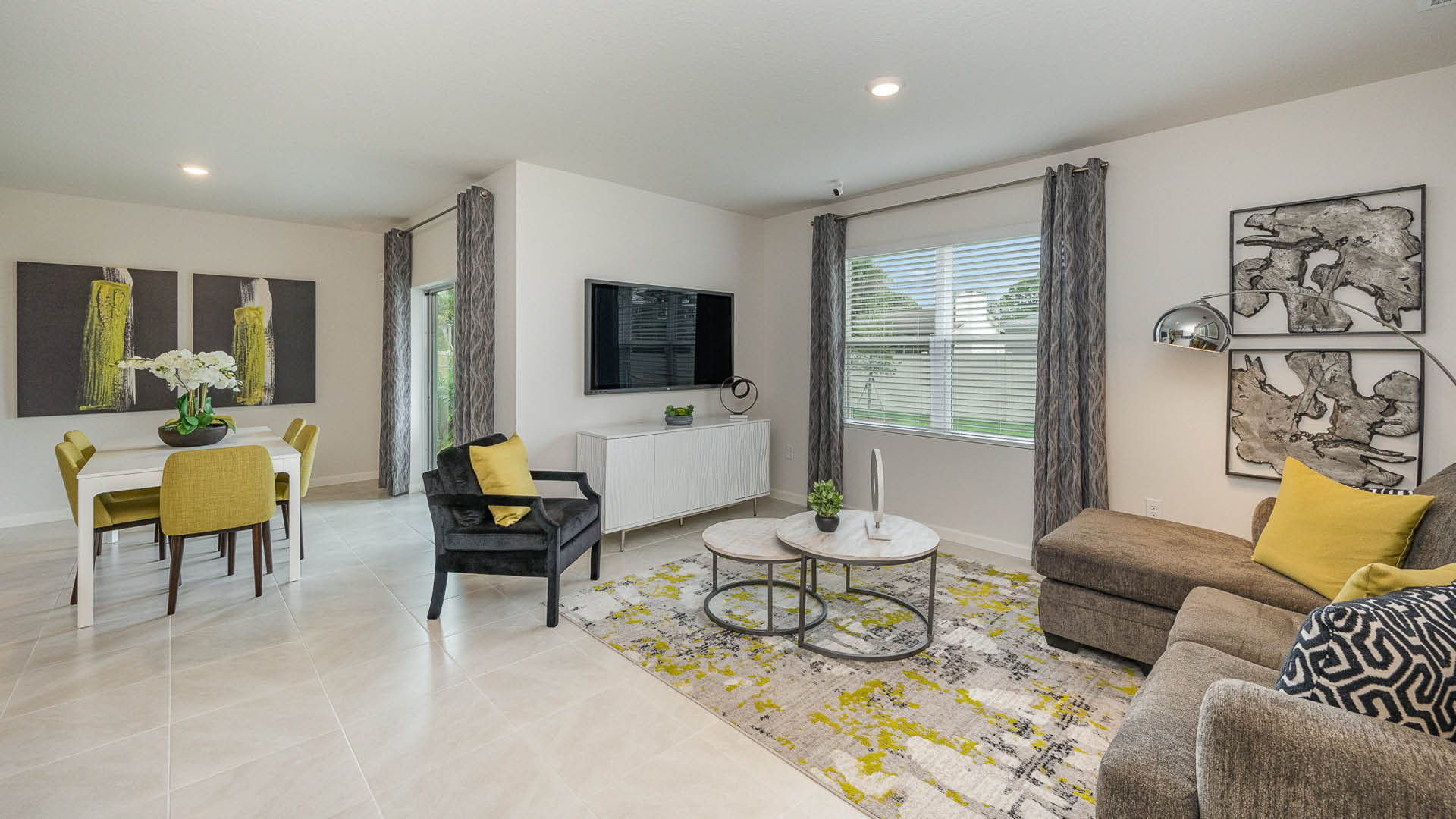 Modern living room and dining area featuring a gray sofa, white table, and vibrant decor with large windows and abstract art.