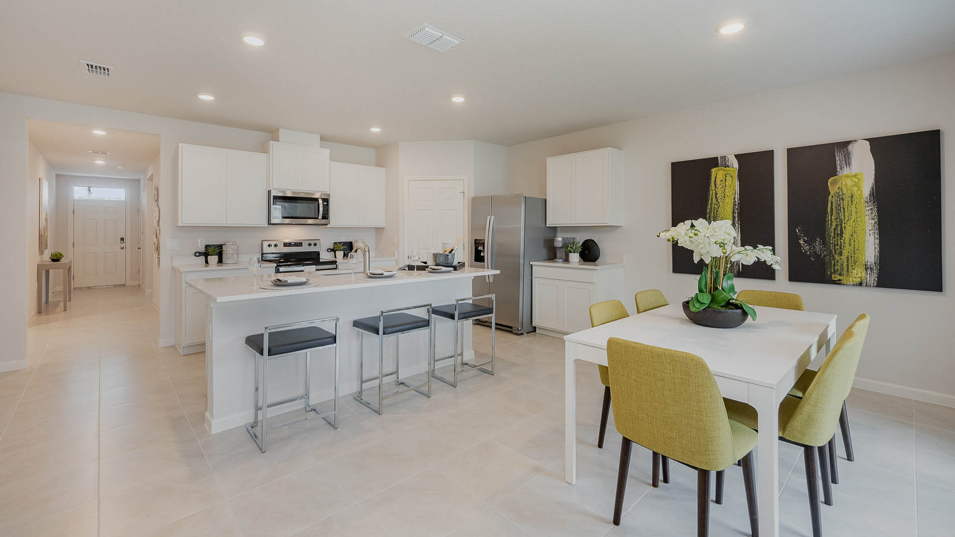 Modern kitchen and dining area featuring sleek cabinetry, stainless appliances, a white table, and stylish green chairs.