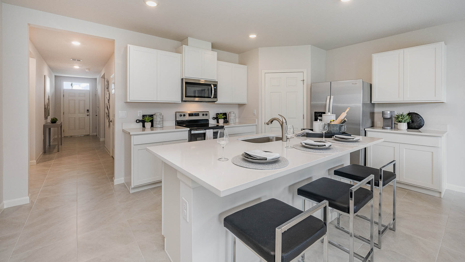 Modern kitchen featuring sleek white cabinetry, stainless steel appliances, a large island with bar stools, and stylish décor.