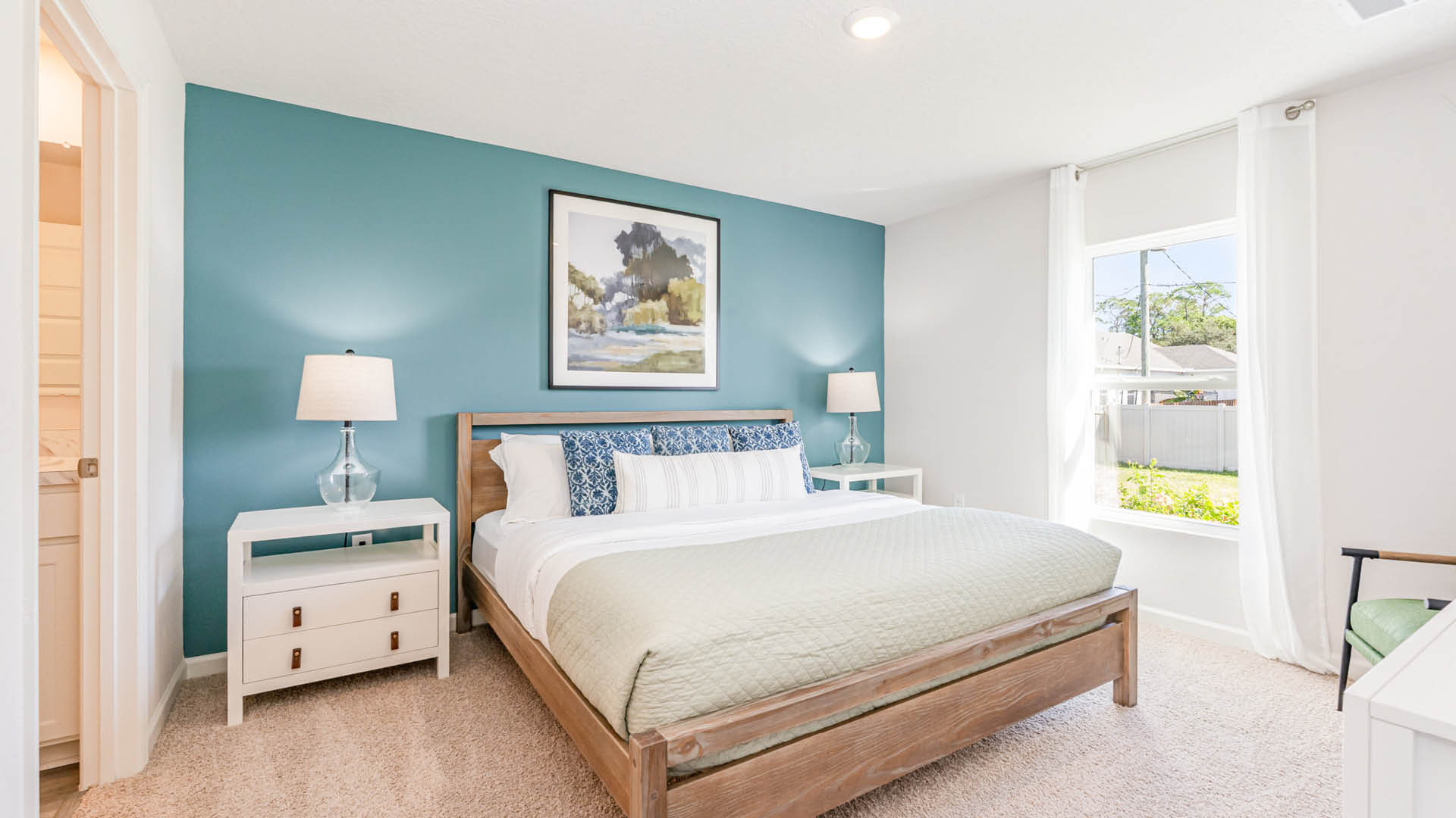 Bright and inviting bedroom featuring a queen bed, teal accent wall, nightstands, and a window with sheer curtains.