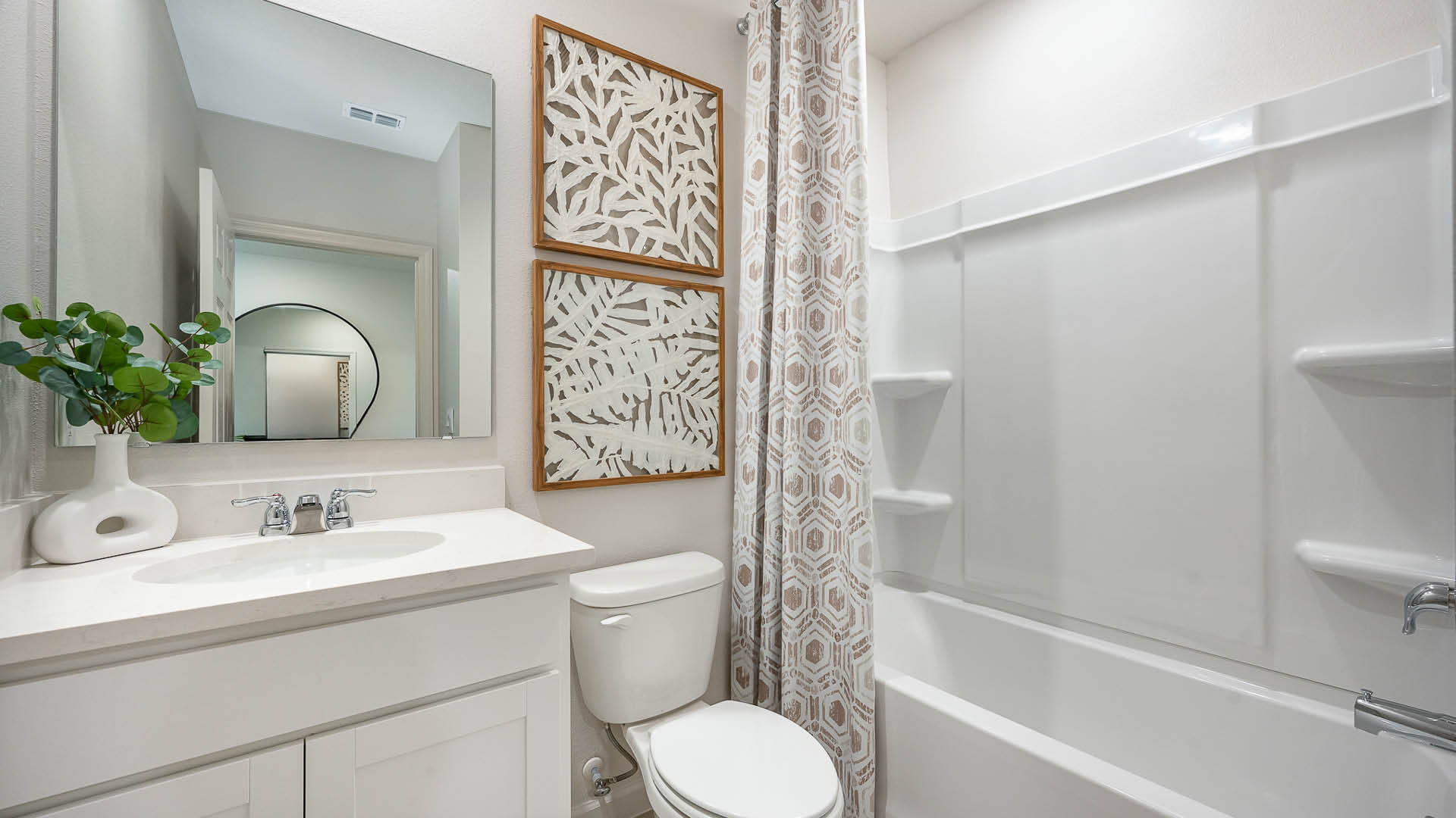 Modern bathroom featuring a white vanity, round mirror, and patterned shower curtain, adorned with decorative wall art.