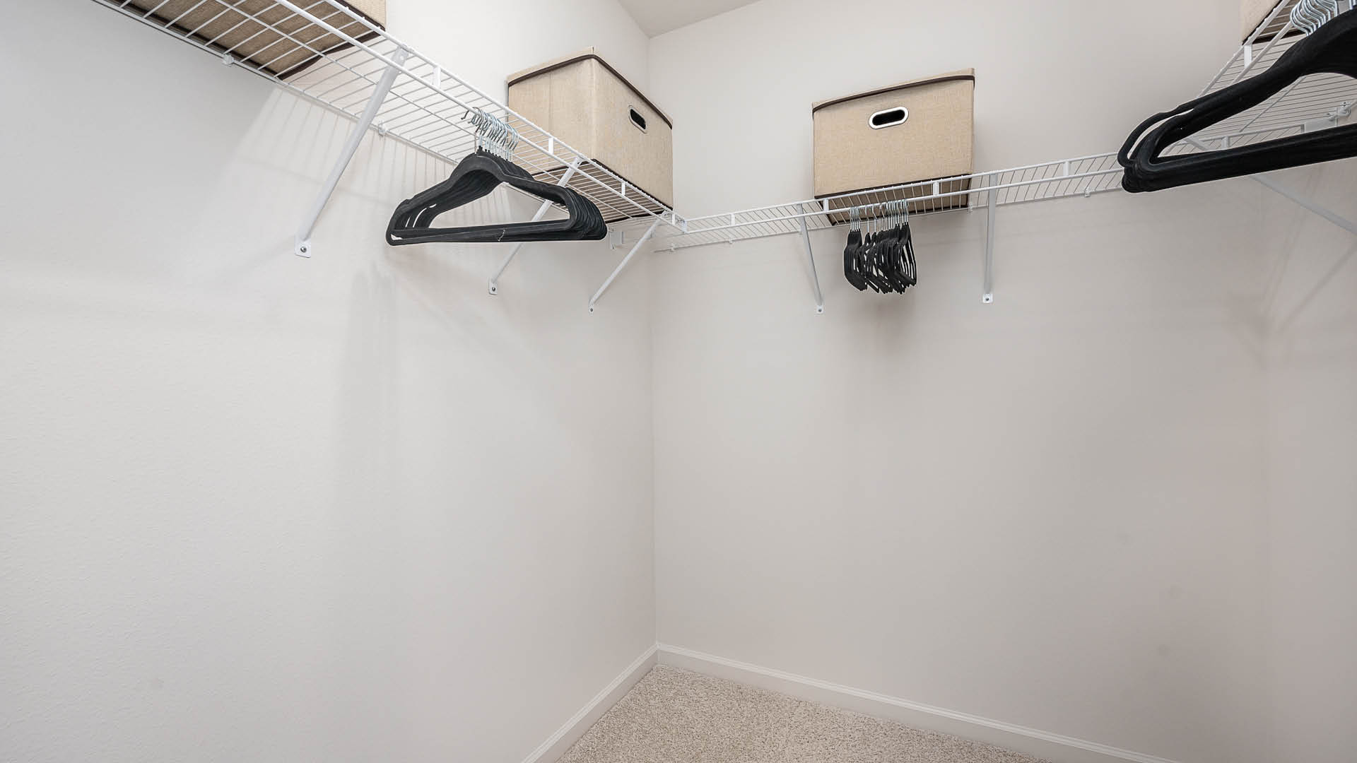 A spacious, uncluttered closet featuring wire shelving, several black hangers, and decorative storage boxes.