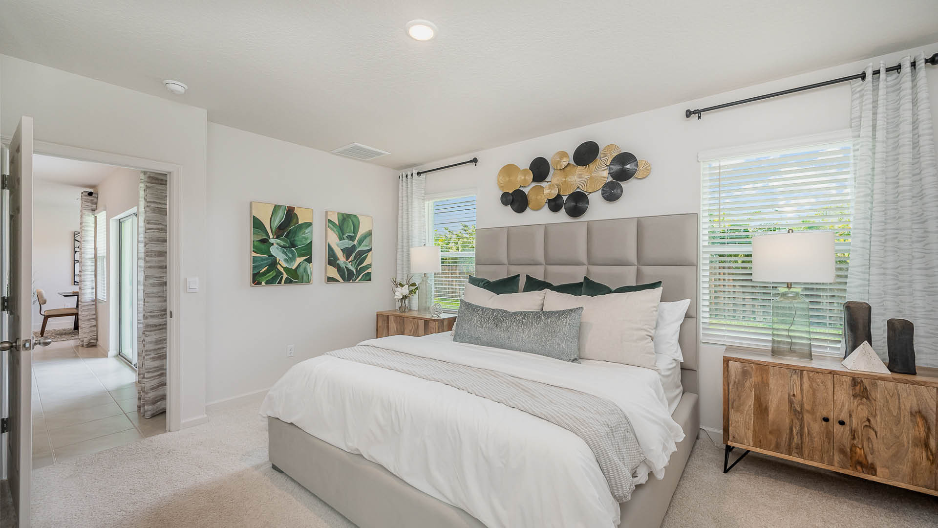Bright and cozy bedroom featuring a plush bed, modern dresser, lounging chair, and green plant decor, with a bathroom entrance visible.