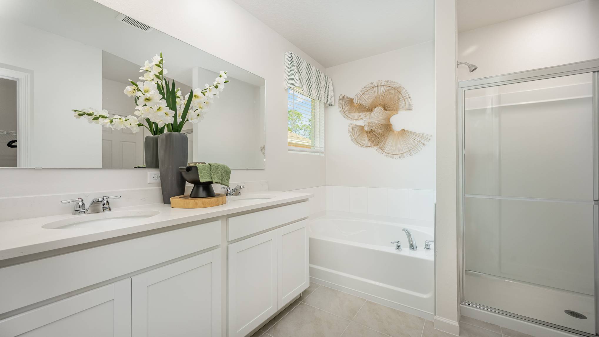 Bright and modern bathroom featuring a double vanity, soaking tub, large mirror, and decorative plants against a light, airy backdrop.