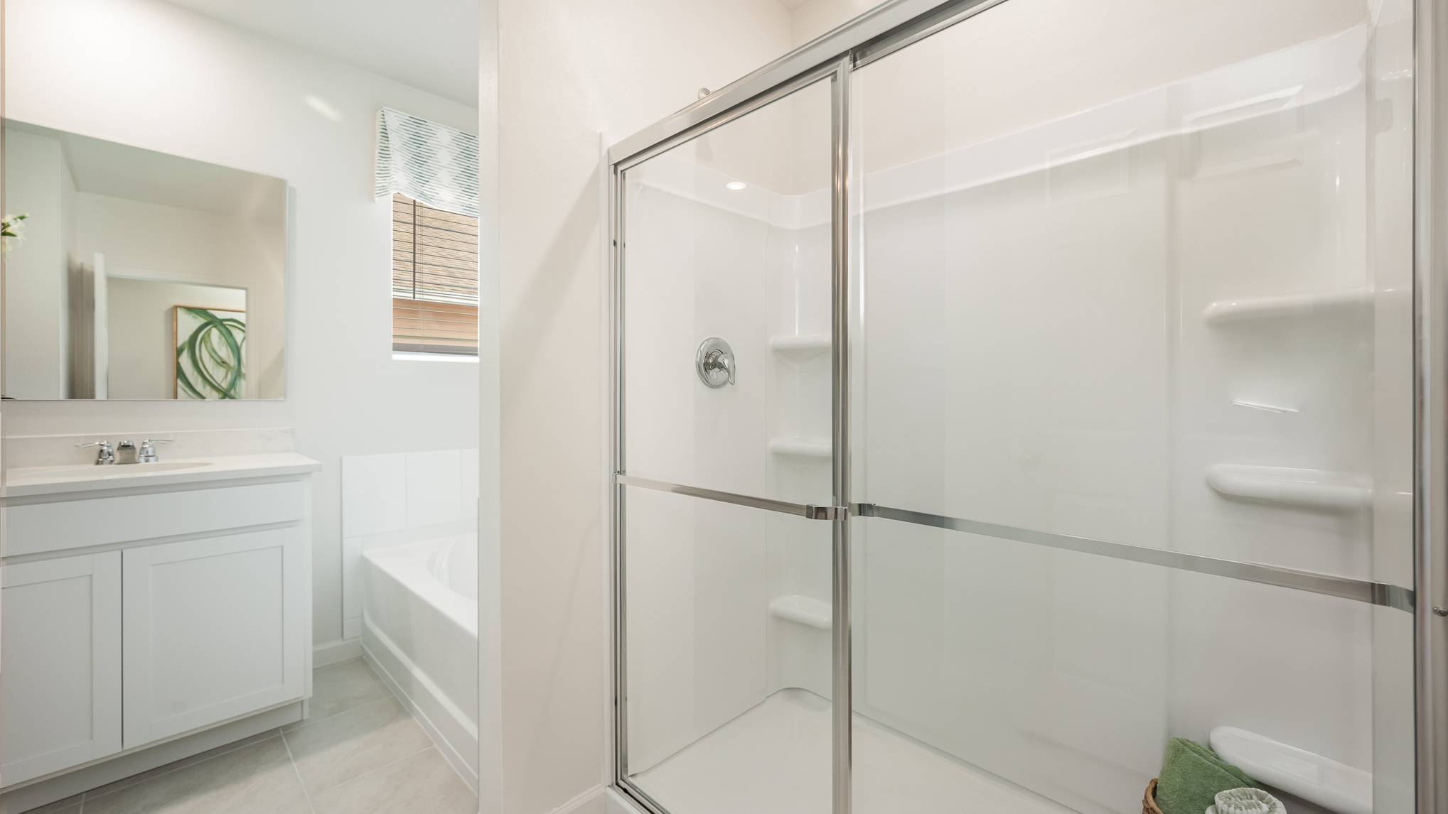 Bright modern bathroom featuring a glass shower, white cabinetry, and a bathtub, with natural light from a nearby window.