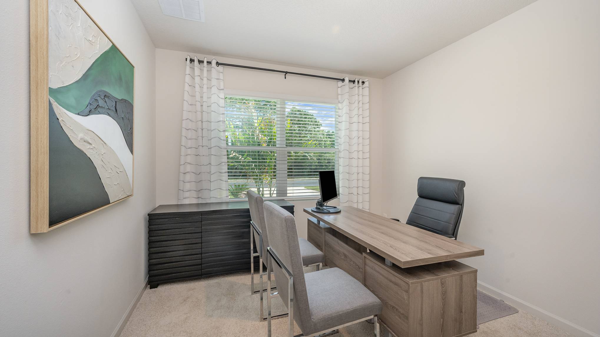 A modern home office featuring a sleek desk, ergonomic chair, two chairs, abstract art, and natural light from a window.
