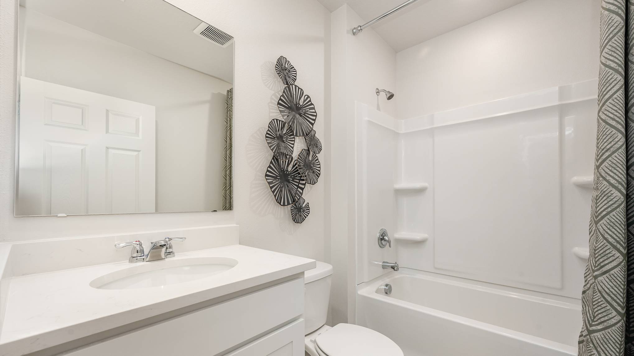 A modern bathroom featuring a white sink, toilet, a mirrored cabinet, and a shower/tub combination with decorative wall art.