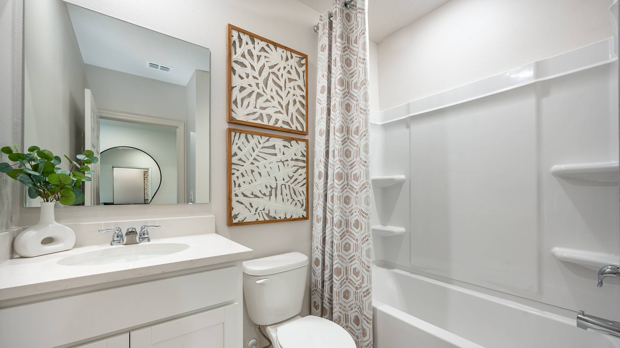 Modern bathroom featuring a white vanity, round mirror, and patterned shower curtain, adorned with decorative wall art.