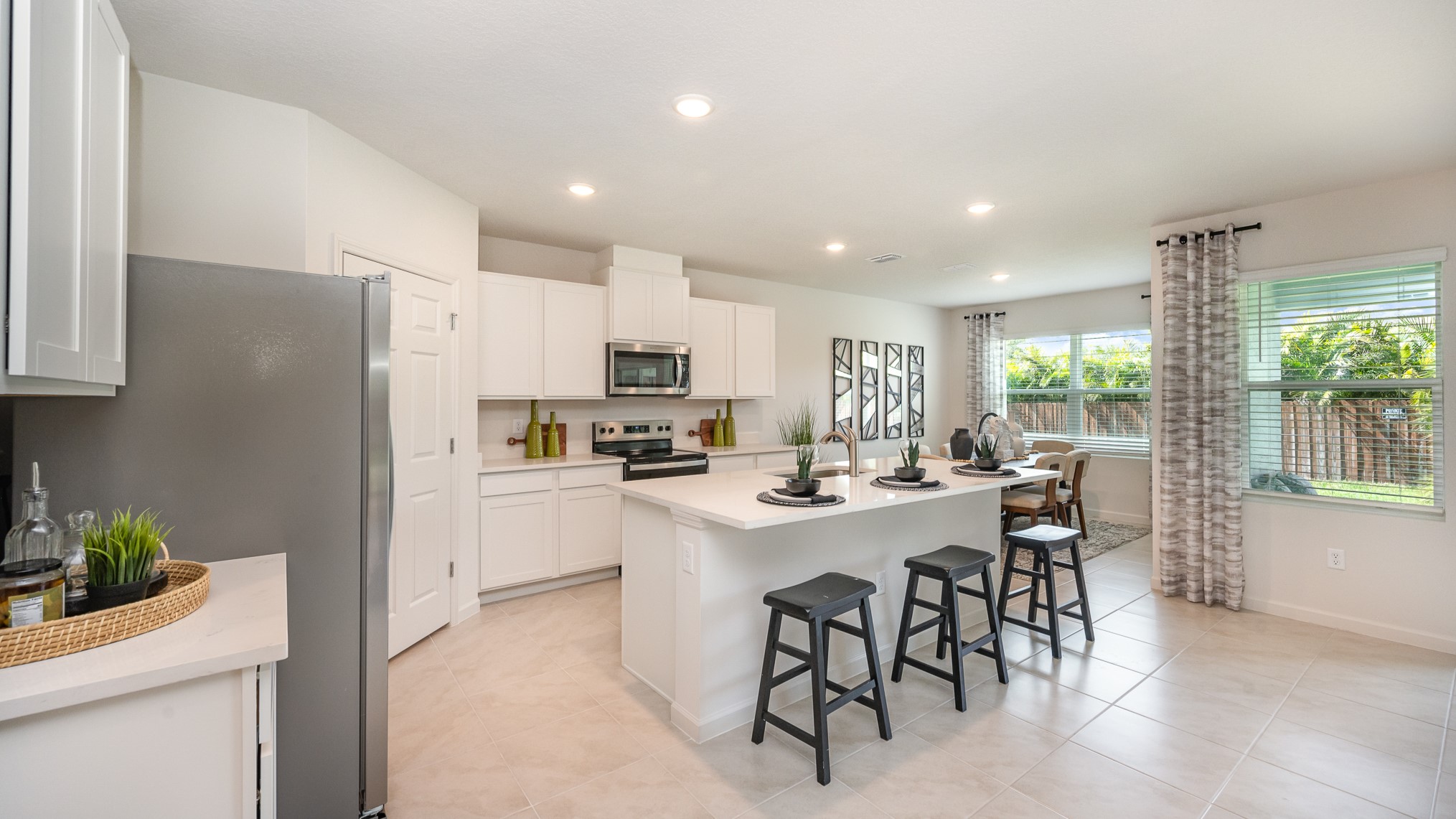 Bright modern kitchen with white cabinets, stainless appliances, and an island with seating; large windows offer a view of the backyard.