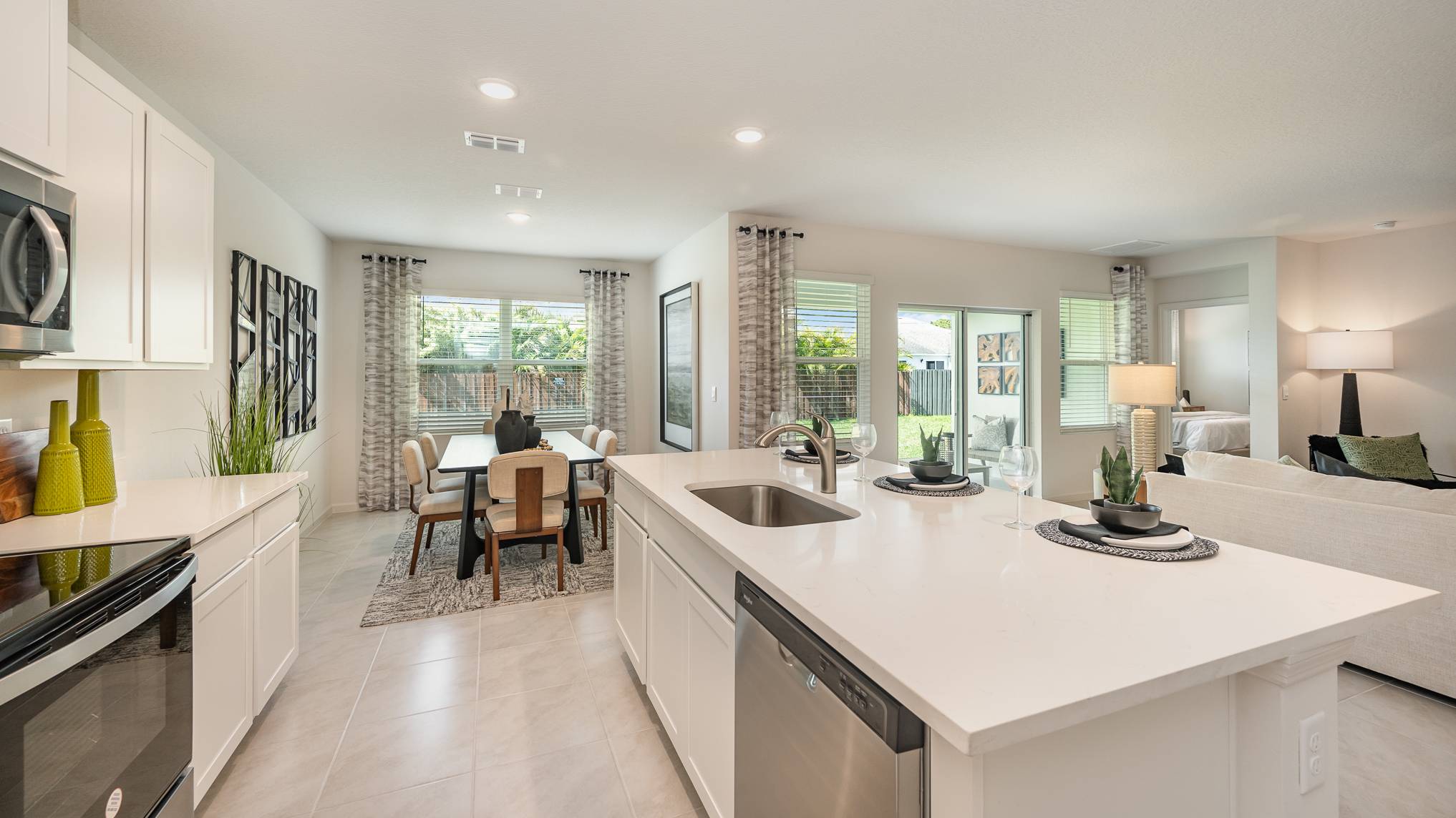 Modern open-concept kitchen and dining area with white cabinetry, stylish decor, and natural light streaming through large windows.
