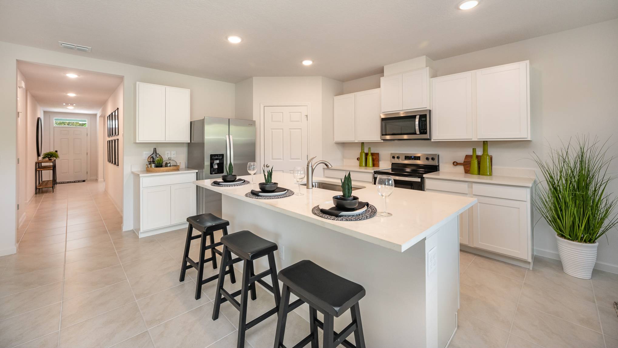 Bright modern kitchen with white cabinets, stainless steel appliances, and a countertop bar with black stools and decor plants.
