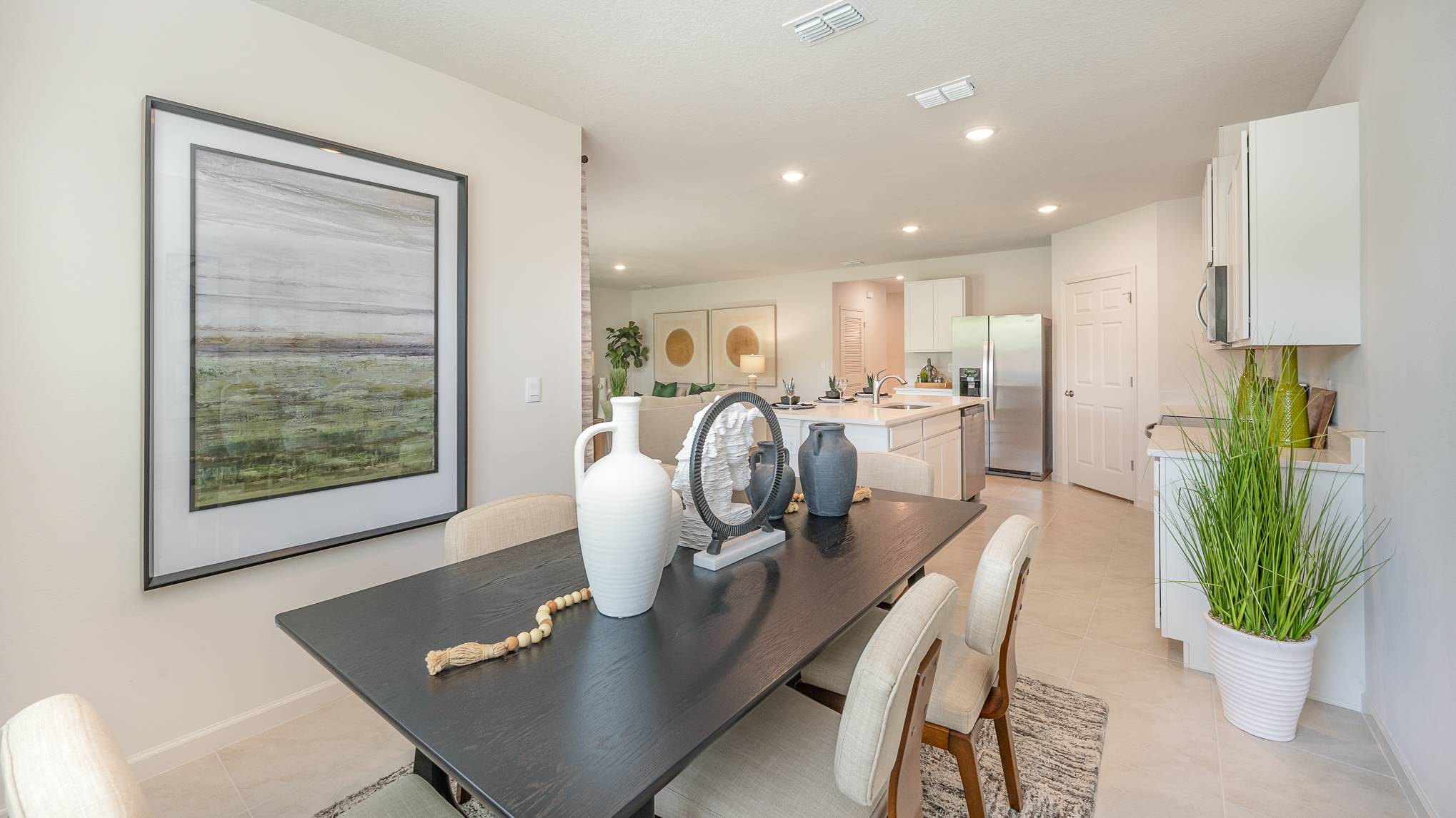 Modern dining area showcasing a black table with vases, stylish chairs, and a bright kitchen in the background.