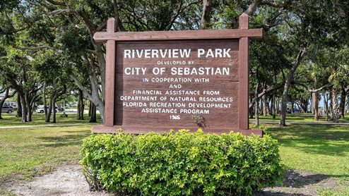A wooden sign for Riverview Park in Sebastian, Florida, surrounded by lush greenery and trees.