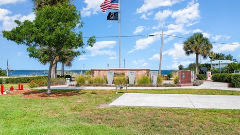 A park memorial honoring veterans from WWII, the Korean War, and the Vietnam War, with flags and a scenic waterfront view.