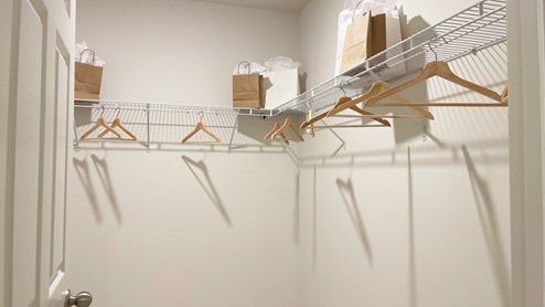 A minimalist closet featuring a wire shelf with paper bags on one side and empty wooden hangers.