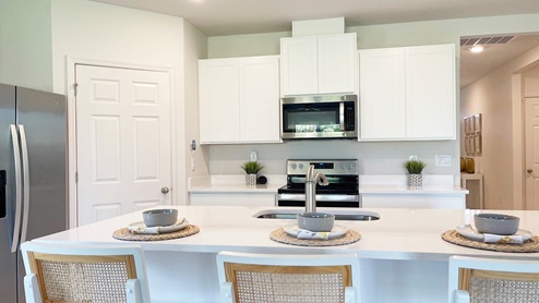 Modern kitchen featuring white cabinetry, stainless steel appliances, a quartz countertop, and breakfast bar with bowls and placemats.