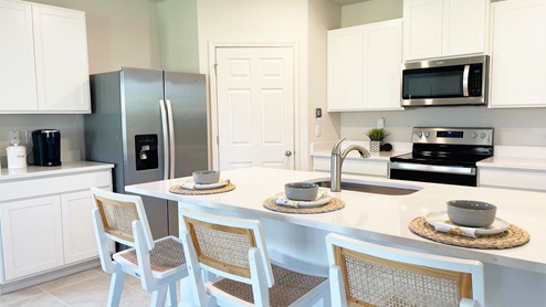Modern kitchen featuring stainless steel appliances, white cabinets, a large island with bowls, and woven placemats. Bright and inviting atmosphere.