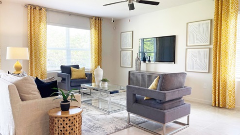 Modern living room with yellow curtains, gray chairs, a glass coffee table, and wall art, featuring a cozy, inviting ambiance.