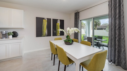 Bright dining room with large white table and six yellow chairs in front of large sliding glass door leading out to the covered lanai.