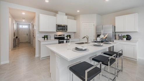 Kitchen with large island, white cabinets, quartz countertops. View of entryway leading to the kitchen.