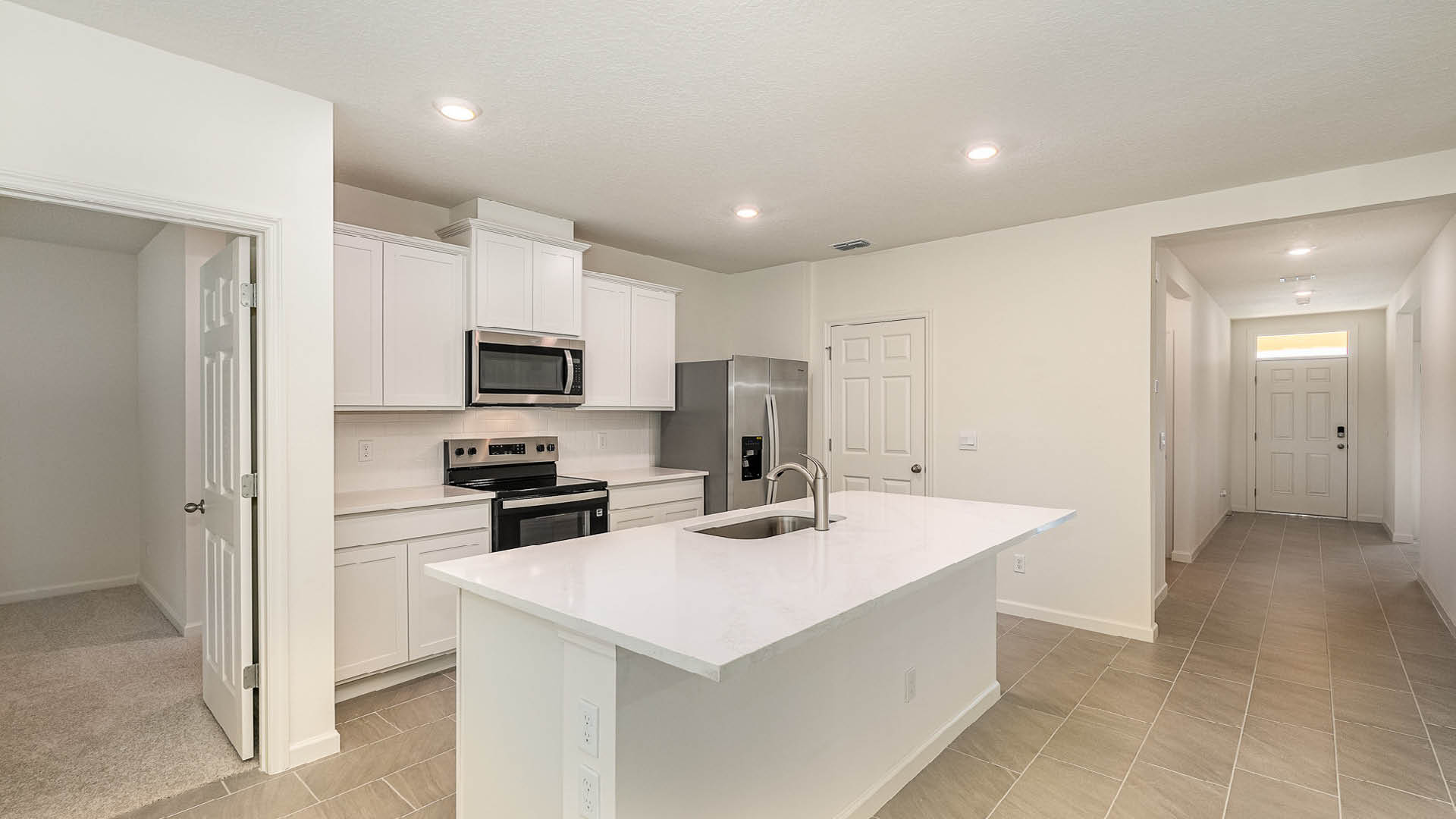 Modern kitchen with white cabinetry, stainless steel appliances, a large island, and access to a hallway leading to the front door.