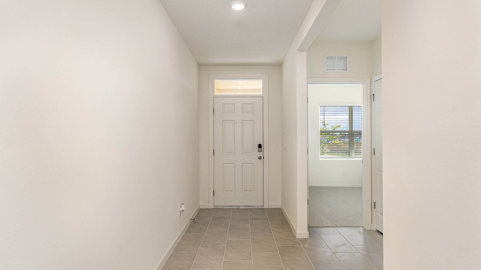 Bright, spacious hallway entrance with a closed front door, tile flooring, and openings to rooms with windows and carpet.