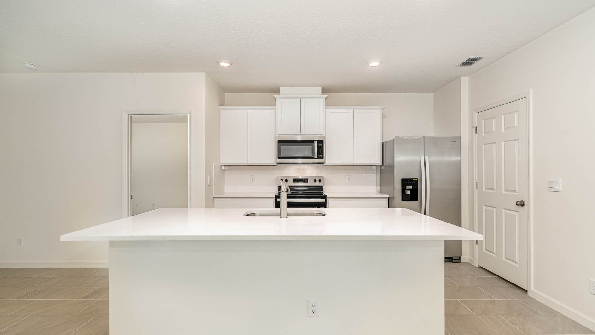 Modern kitchen featuring white cabinets, stainless steel appliances, and a large island with a sink, in a bright, open space.